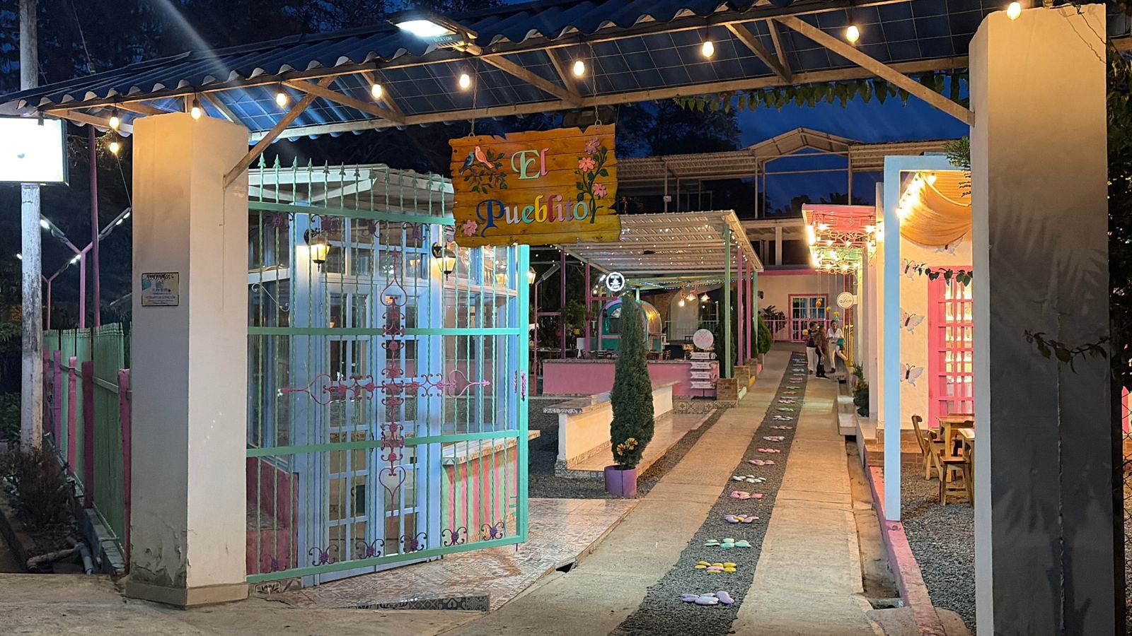 Entrada de El Pueblito de Colores de noche, con su letrero de madera y luces