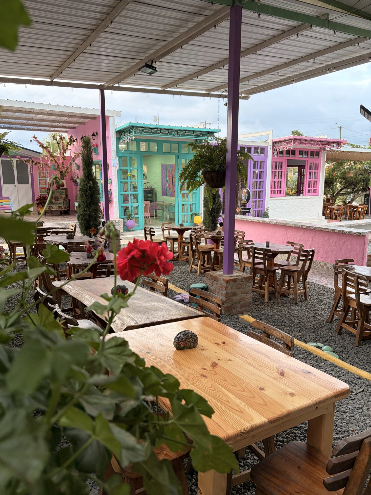 Mesas de madera en la plazoleta de El Pueblito con flores y casitas de colores